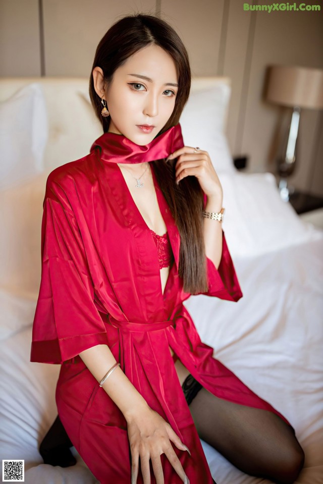 A woman in a red robe sitting on a bed.