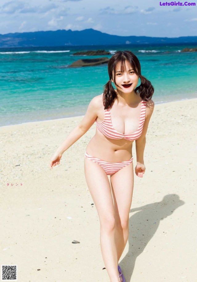 A woman in a red and white striped bikini walking on a beach.