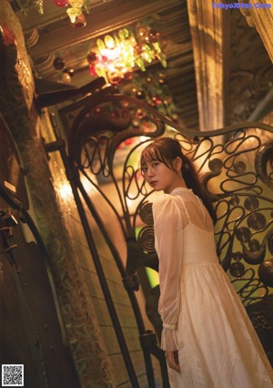 A woman in a white dress leaning against a wall.