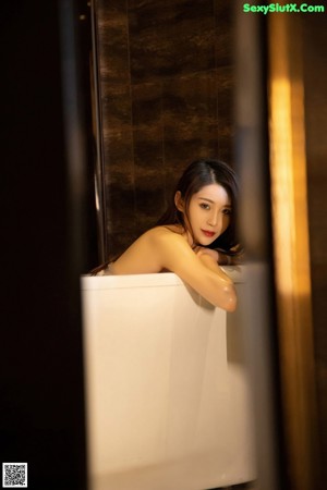 A woman in a white lingerie sitting in a bathtub.