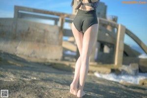 A woman in a bathing suit sitting on a rock by the ocean.