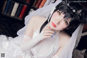 A woman in a wedding dress sitting on a chair in front of a bookcase.