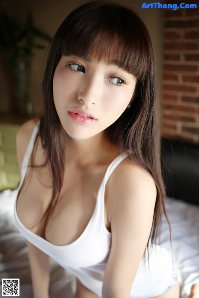 A woman in a white tank top sitting on a bed.