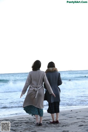 Two women walking along a pier with a mountain in the background.