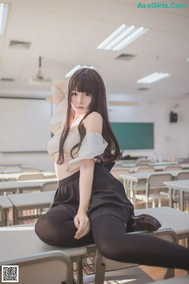 A woman sitting on a desk in a classroom.