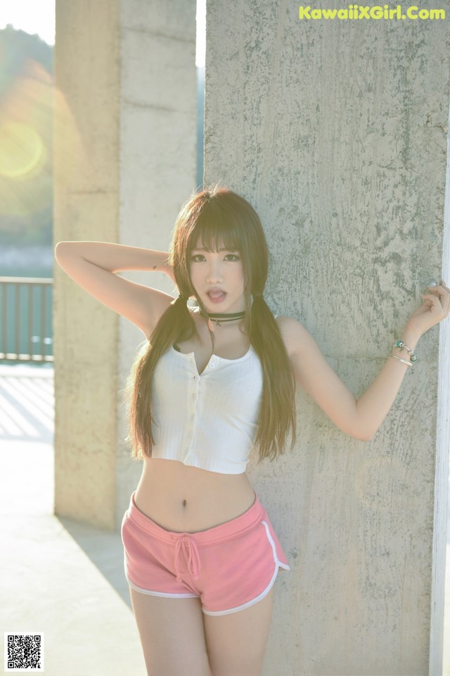 A young woman leaning against a wall with her hands on her hips.