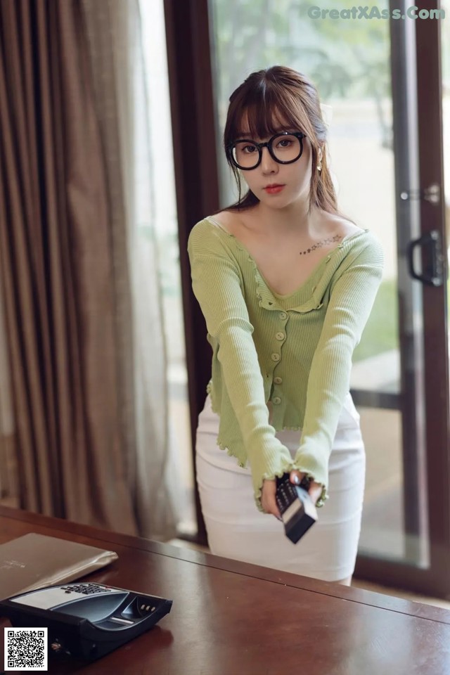 A woman wearing glasses standing in front of a desk.