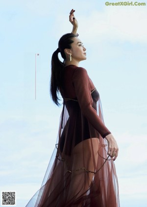 A woman in a gray dress standing in front of a white wall.