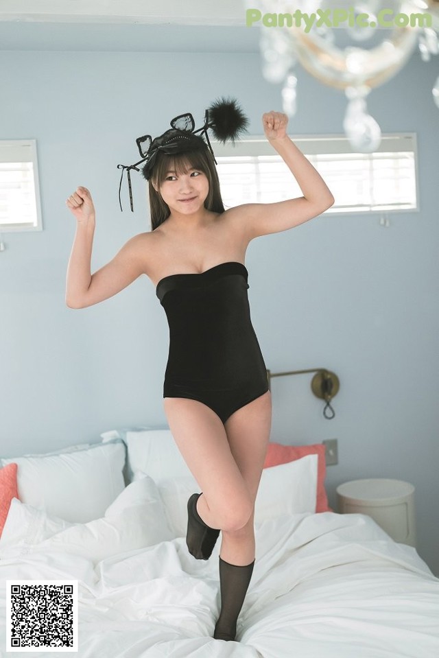 A woman in a black bodysuit jumping on a bed.