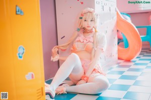 A woman in a pink bikini leaning against a locker.