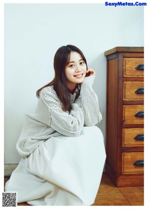 A woman sitting on the floor in front of a dresser.