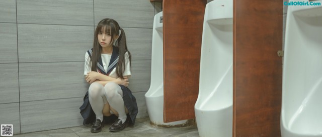 A woman sitting on the floor in front of urinals.