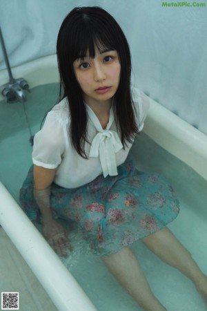 A woman in a white shirt and blue skirt sitting in a bathtub.