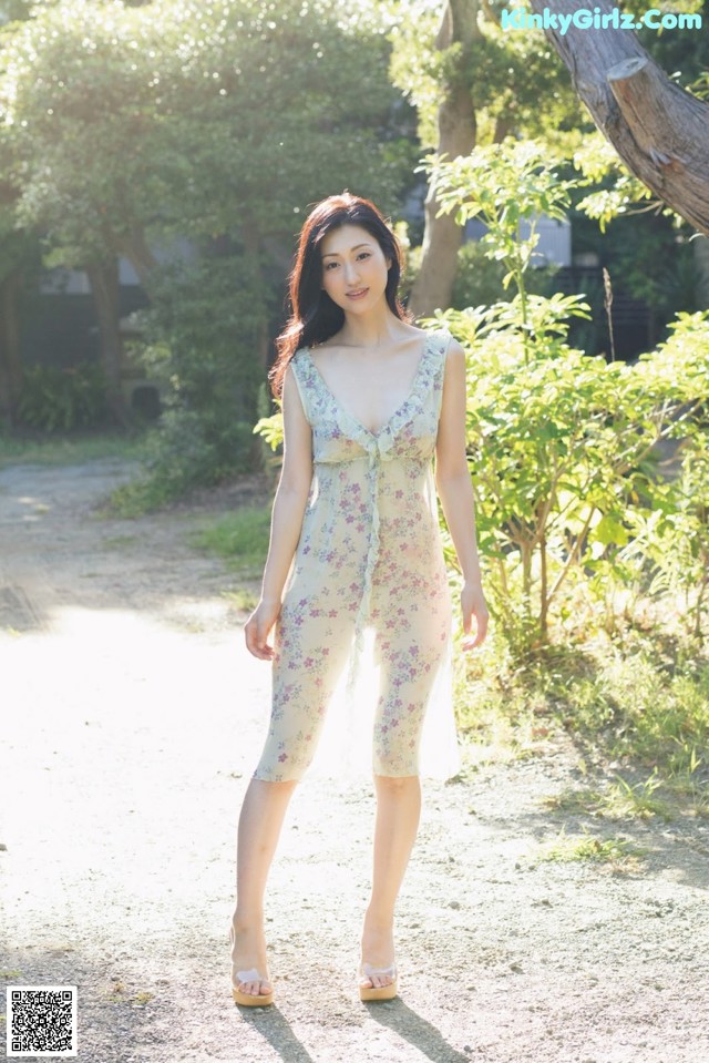 A woman in a floral dress standing on a dirt road.